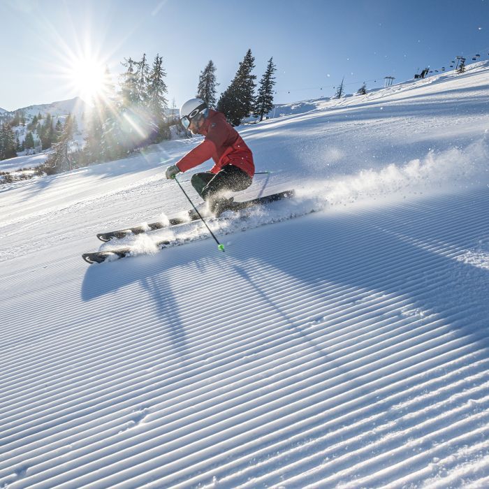 Skifahrer zieht die ersten Schwünge auf der frisch präparierten Piste