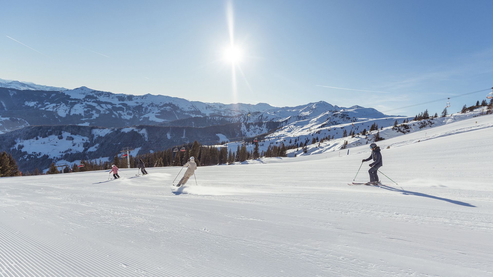 Familie fährt auf einer sonnigen Piste mit Bergpanorama im Ski Juwel