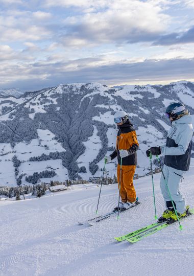 Zwei Skifahrer genießen auf der Piste den Blick über die verschneiten Berge