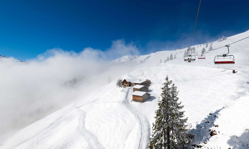 Verschneite Almhütte und Sessellift über dem Nebelmeer am Schatzberg