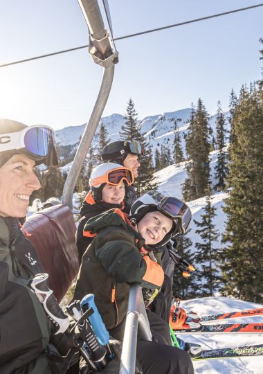Familie mit lachenden Kindern fährt mit der Sesselbahn ins Skigebiet